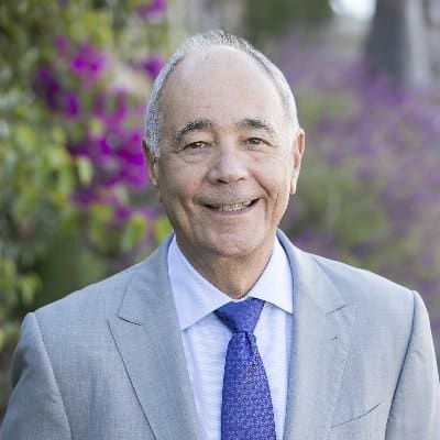 Ken Sigelman smiling in a flower garden with a gray suit and blue tie on