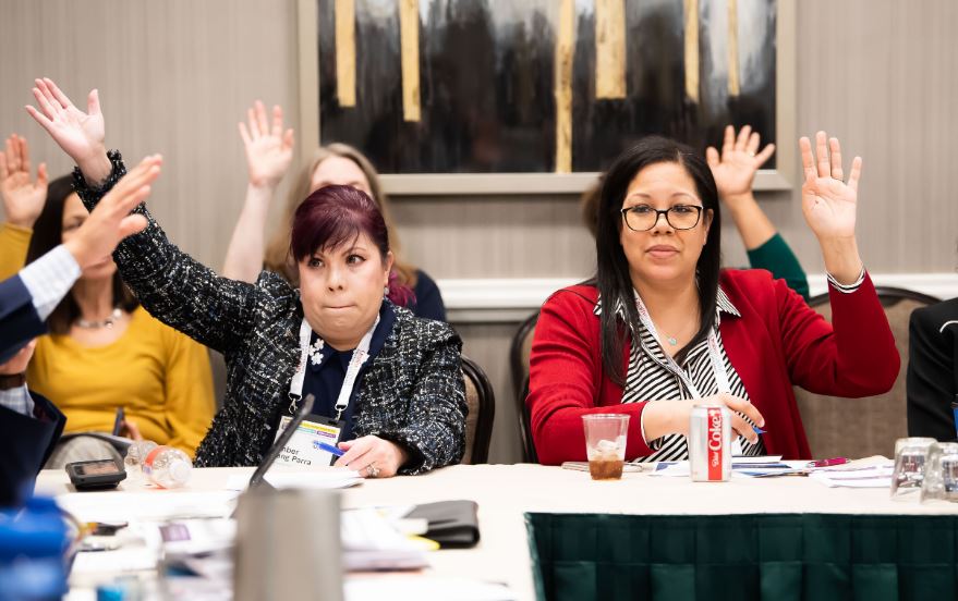 Two female caucus meetings raising their hands to vote at a caucus meeting.
